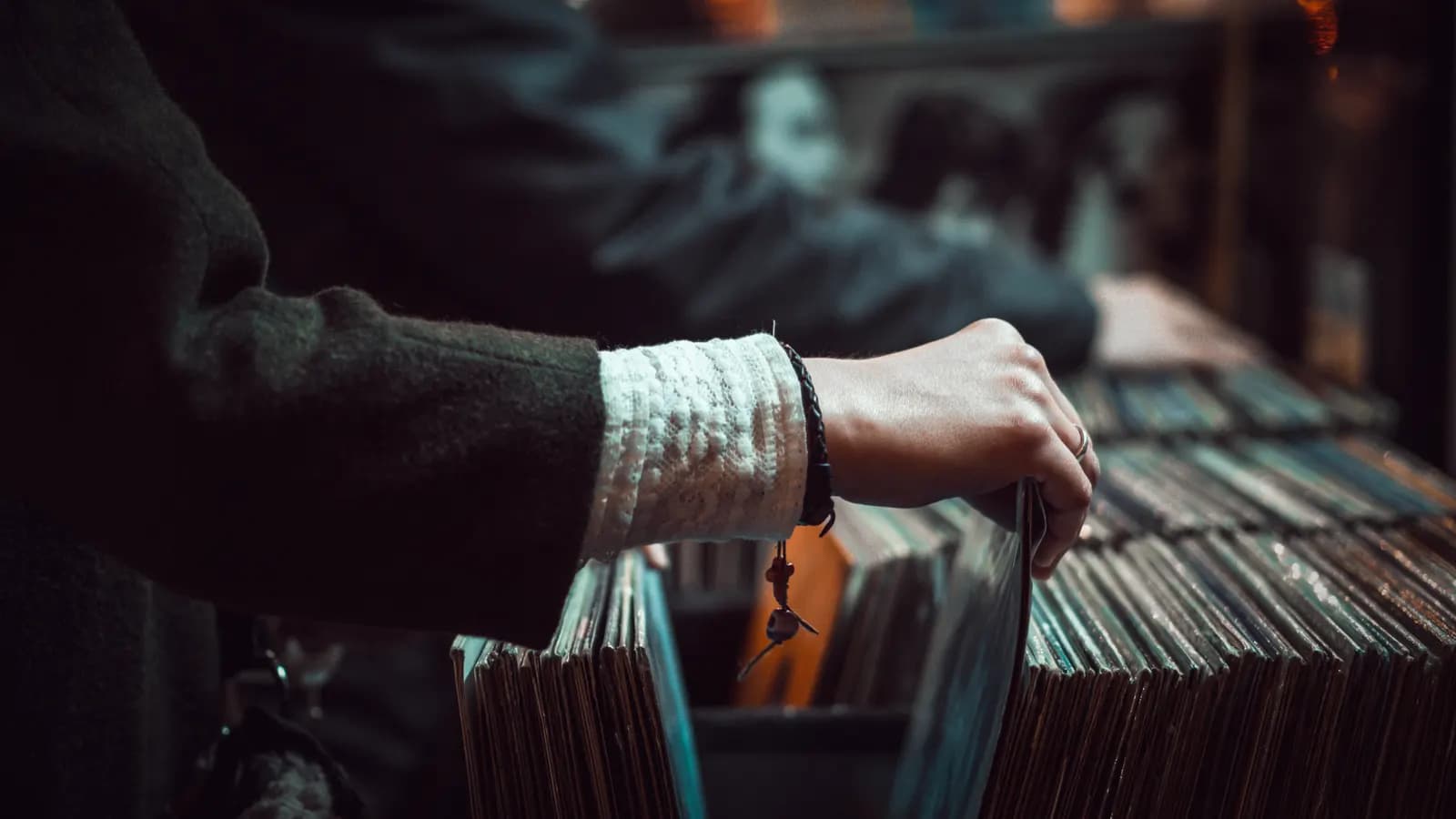 Close view of a person's hands flipping through records in a shop, teal shadows and warm highlights.